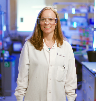 Hymyilevä nainen laboratoriovarustus päällään pitelee papereita käsissään.