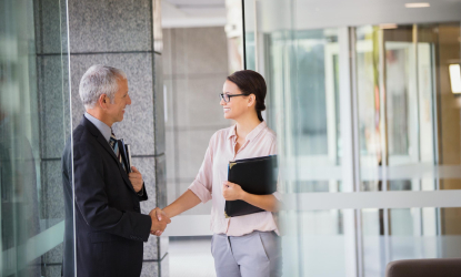 Kaksi ihmistä kättelee toimistossa, symboloi luotettavuutta, etiikkaa ja komplianssia