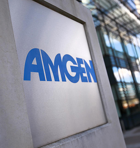 Amgen logo in foreground against glass building – Amgen-logo lasirakennuksen edessä kivijalassa.